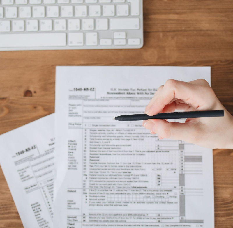 A hand holding a pen over income tax return forms beside a keyboard